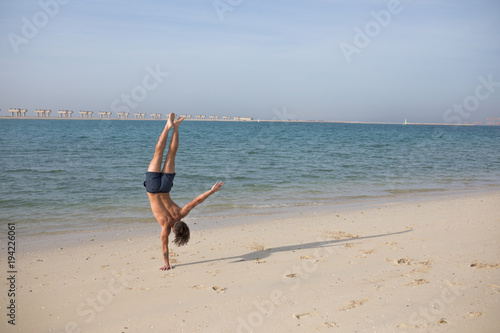 Young man doing handstand on the beach.