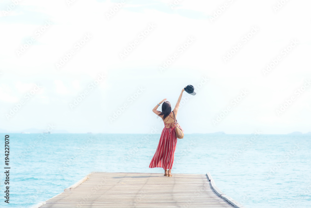 Summer Day. Smiling women relax and wearing red dress fashion standing on the wooden bridge over the sea, blue sky background. Travel and Vacation. Freedom Concept Summer Day. Smiling women relax and wearing red dress fashion standing on the wooden bridge over the sea, blue sky background. Travel and Vacation. Freedom Concept