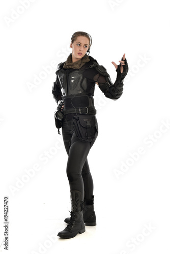 full length portrait of female soldier wearing black tactical armour with arms raised, isolated on white studio background.