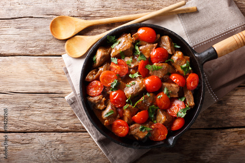 Veal in spicy sauce with cherry tomatoes and greens close-up in a pan. horizontal top view