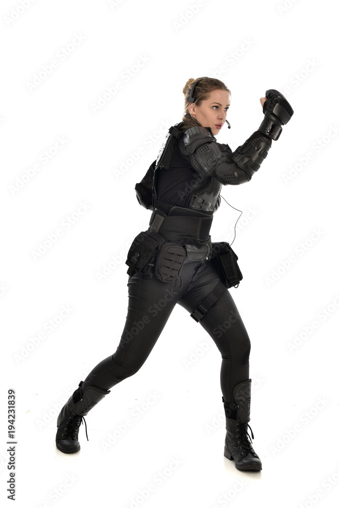 full length portrait of female  soldier wearing black  tactical armour with arms raised, isolated on white studio background.