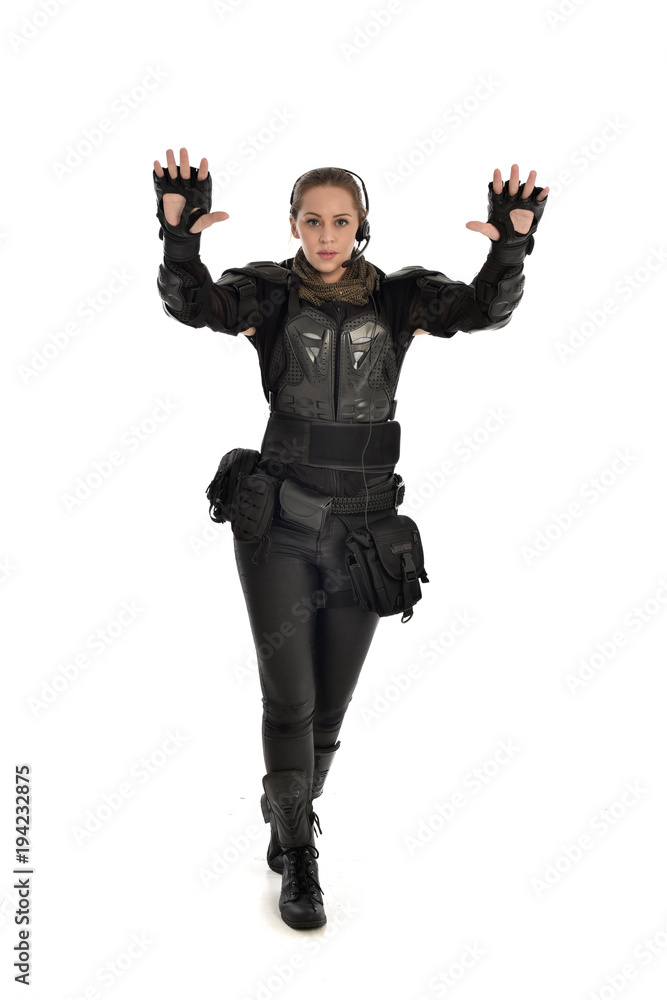 full length portrait of female  soldier wearing black  tactical armour with arms raised, isolated on white studio background.