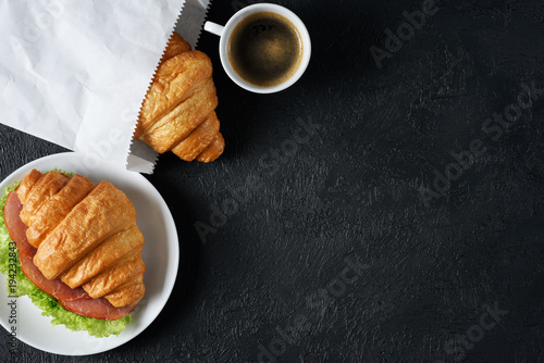 Croissant with ham and lettuce, coffee on a dark background. Breakfast flat lay.