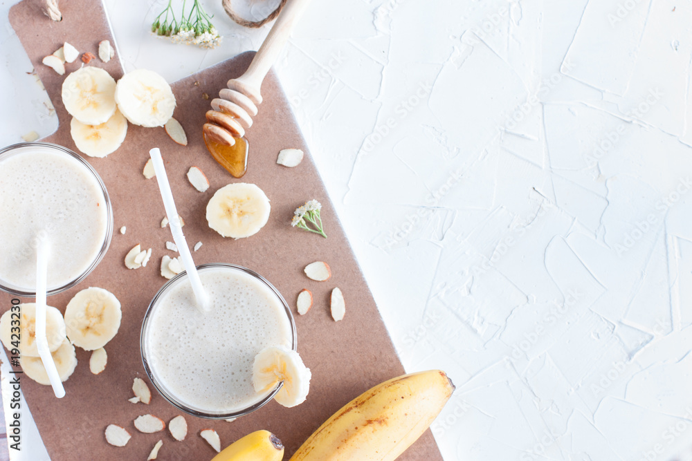 Banana smoothie with banana, milk, almonds and honey in glass glasses on a white table, top view, horizontal, selective focus Banana smoothie with banana, milk, almonds and honey in glass glasses on a white table, top view, horizontal, selective focus