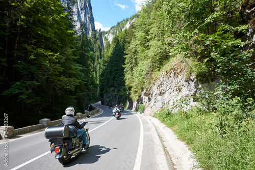 Tourists bikers traveling in motorcycles on mountain road in Bicaz Canyon, Romania between high vertical rocky cliffs. One of the most spectacular roads in Romania. Adventure and travel theme. photo