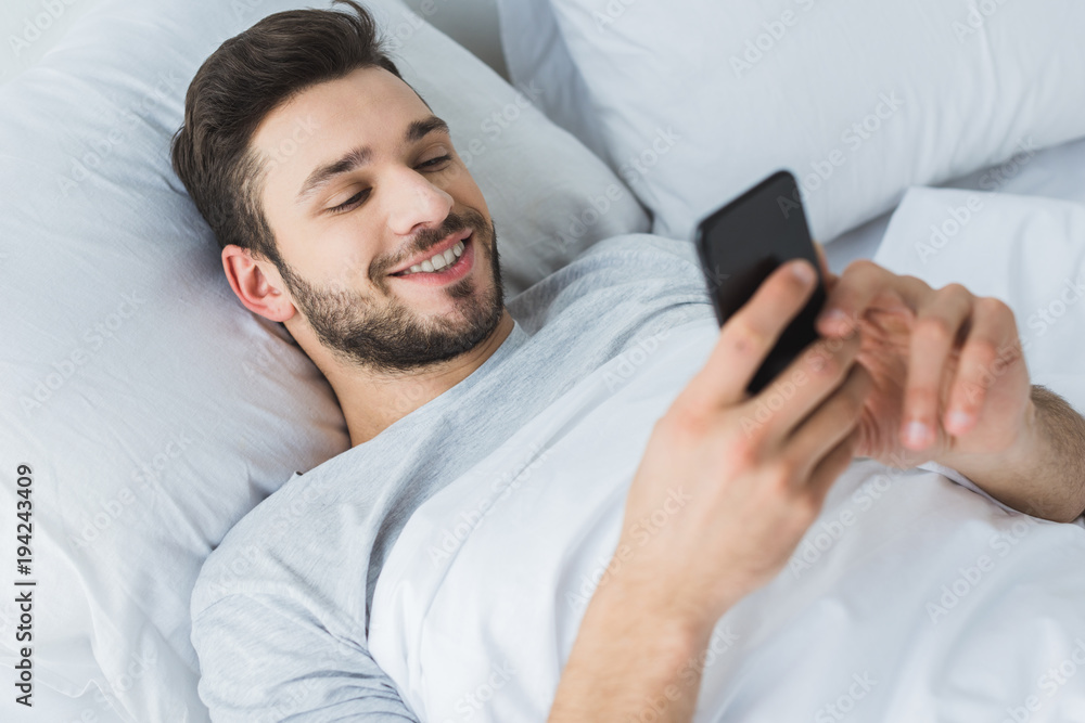 happy bearded man using smartphone in bed in the morning happy bearded man using smartphone in bed in the morning