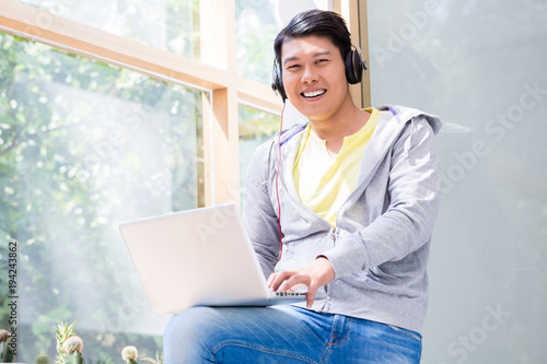 Portrait of Chinese young man wearing casual clothes while using a laptop in a modern office or at the university