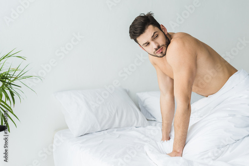 handsome shirtless man posing on white bed in the morning