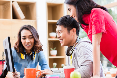 Successful professional team of web designers smiling while testing responsive layout on both mobile phone and desktop PC