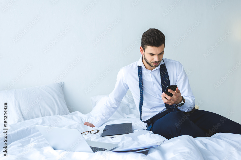 businessman working with smartphone, documents and laptop on bed in morning businessman working with smartphone, documents and laptop on bed in morning