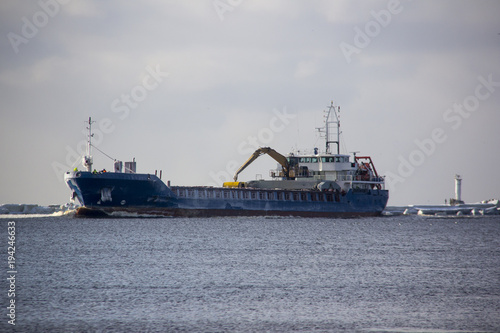 Logistics and transportation Cargo ship with ports crane bridge coming in port and transportation industry winter suny day in Latvia baltic sea an river daugava.