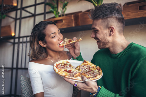 Mixed race couple eating pizza in modern cafe. They are laughing and eating pizza and having a great time.