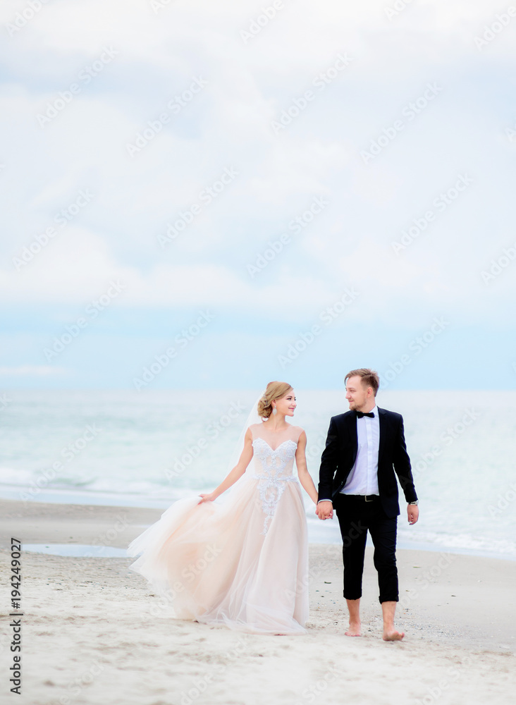 Bride and groom hold each other hands tender walking along the beach by the sea Bride and groom hold each other hands tender walking along the beach by the sea