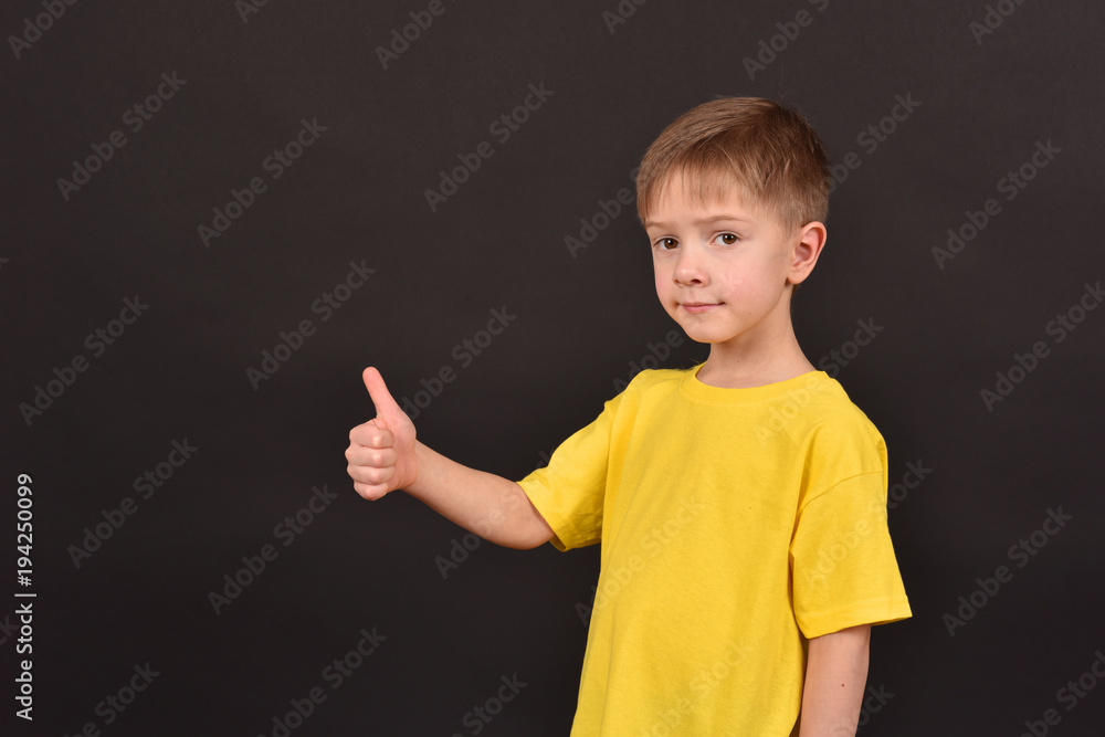 Cheerful boy on a black background. Happy childhood. A child in a yellow T-shirt. Children on a dark background. Cheerful boy on a black background. Happy childhood. A child in a yellow T-shirt. Children on a dark background.