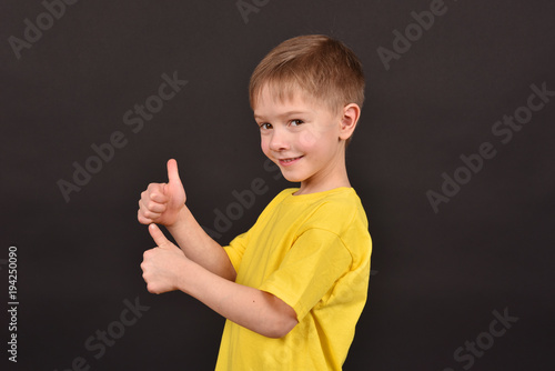 Cheerful boy on a black background. Happy childhood. A child in a yellow T-shirt. Children on a dark background.