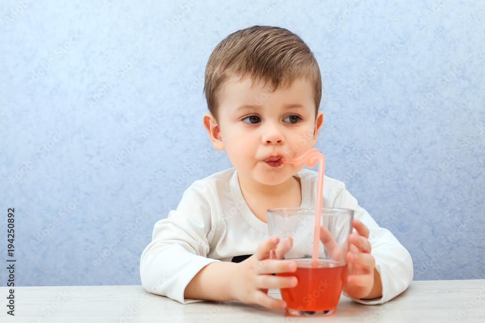 Cute little boy drinking juice on light blue background. Lovely kid drink grape juice. Cute little boy drinking juice on light blue background. Lovely kid drink grape juice.