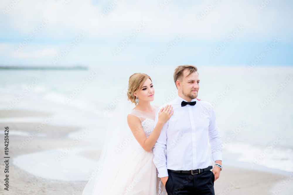 Bride stands behind groom facing the wind on beach Bride stands behind groom facing the wind on beach