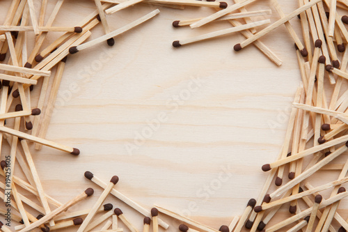 wooden unburned matches with black heads scattered against a light brown wood. empty space in the center