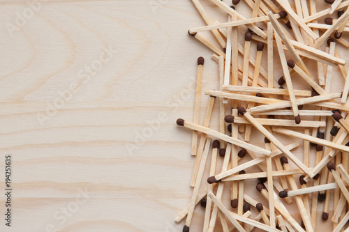 wooden unburned matches with black heads scattered against a light brown wood. empty space left
