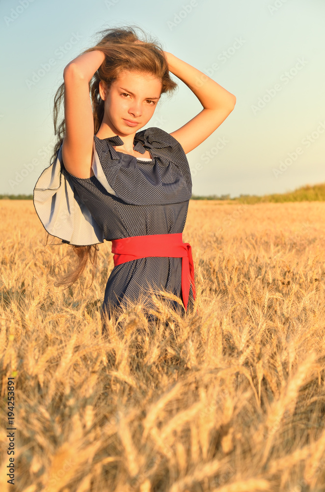 A young woman stands among the ears in the field under the sun