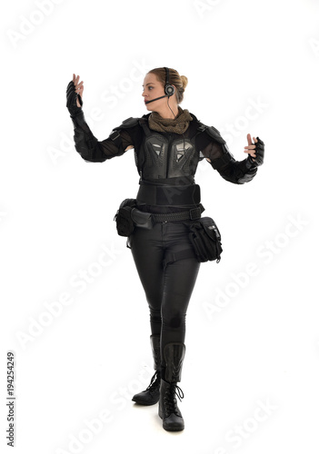full length portrait of female  soldier wearing black  tactical armour with arms raised  isolated on white studio background.
