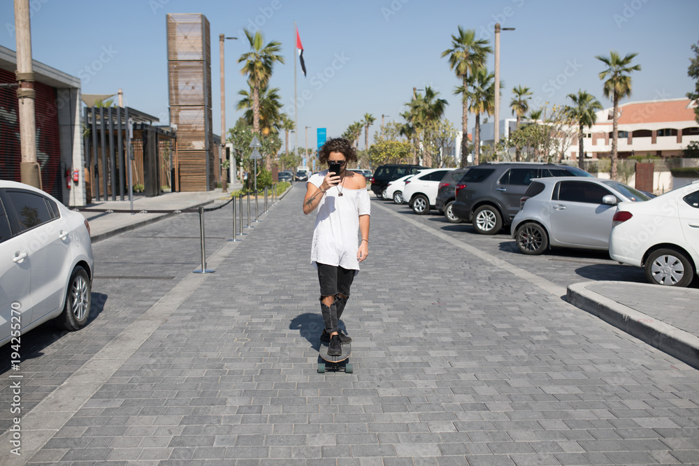 A young man in a white t-shirt riding a skateboard on the street.