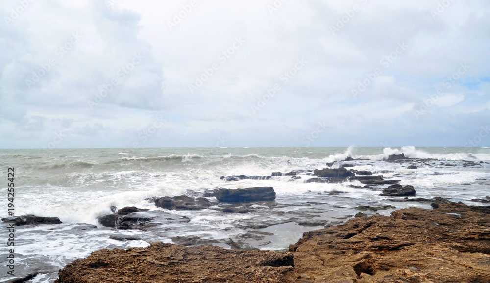 the view from the shore of the raging ocean during a storm, in the Spanish city of Cadiz, large waves crash on rocks and stones.