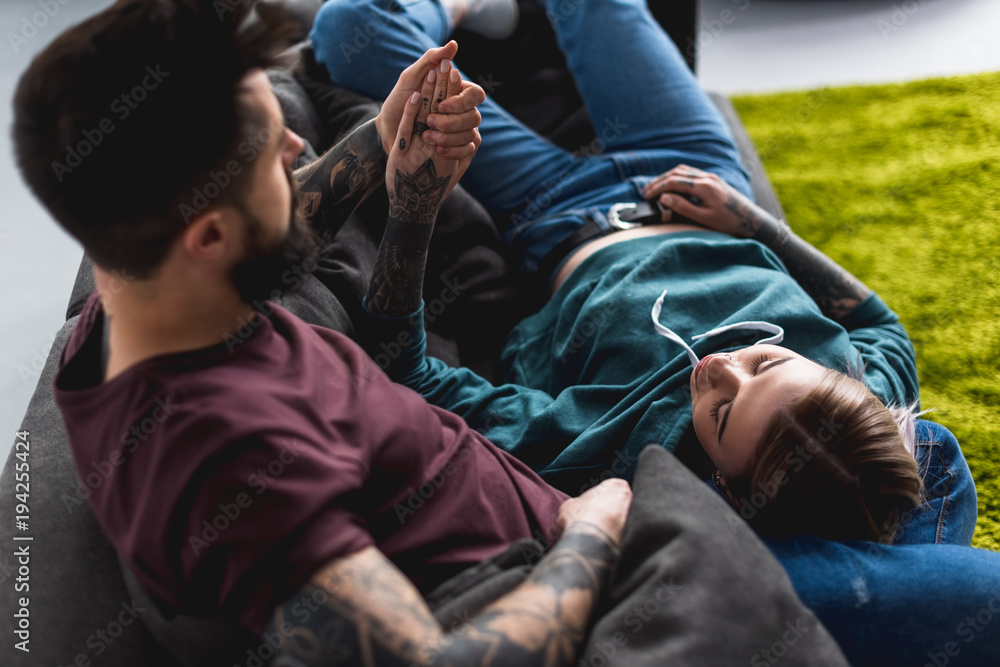 tattooed couple lying on sofa and holding hands