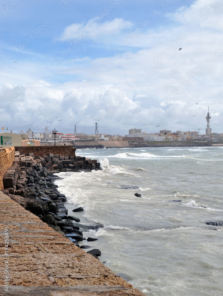 the view from the shore of the raging ocean during a storm, in the Spanish city of Cadiz, large waves crash on rocks and stones.