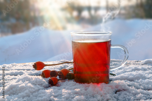 hot red tea from hibiscus and rose hip fruits outdoors in the snow with sunbeams, healthy warming drink for immunity protection against cold and flu, copy space