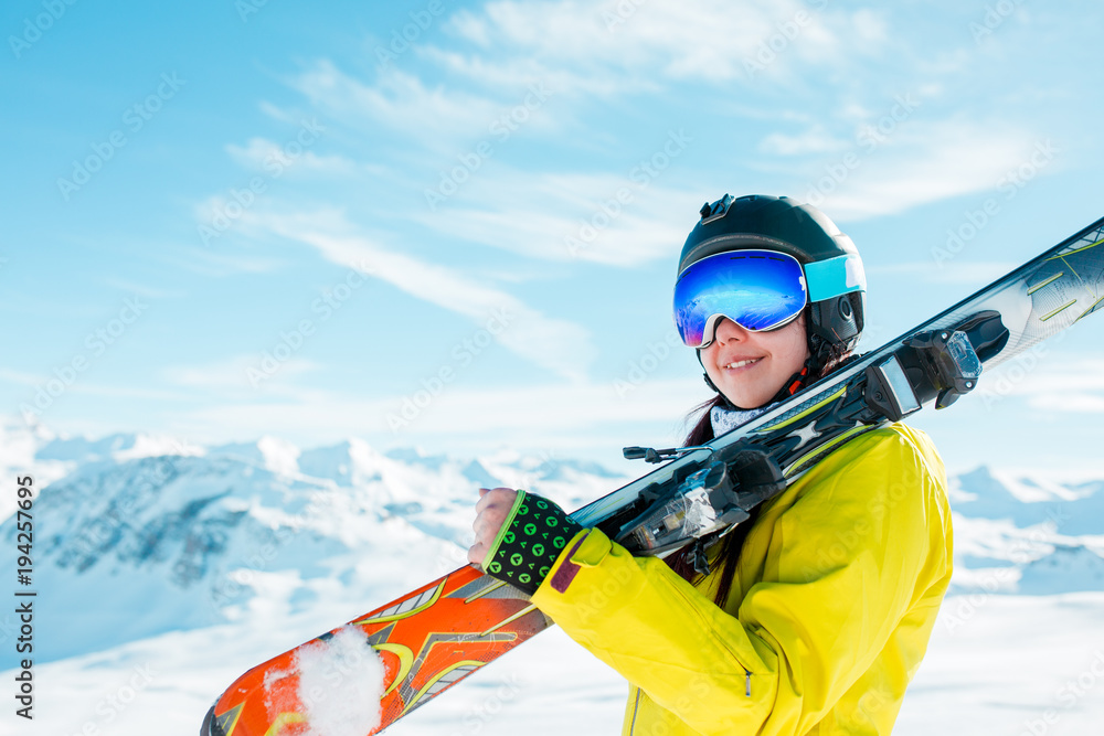 Picture of sports woman in helmet with skis on her shoulder against background of winter hills Picture of sports woman in helmet with skis on her shoulder against background of winter hills