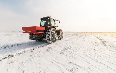 Farmer with tractor seeding - sowing crops at agricultural fields in winter