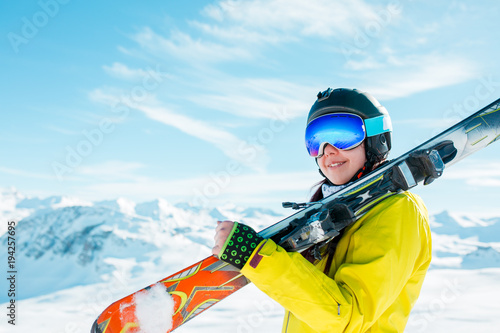 Picture of sports woman in helmet with skis on her shoulder against background of winter hills