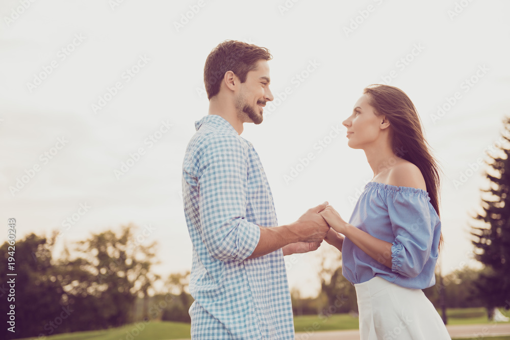 Fototapeta premium Side profile view of bearded brunet guy in checkered shirt, bonding dreamy lady, looking deep into eyes of each other. Leisure, chill, lawn stroll, relax lifestyle, well dressed stylish partners