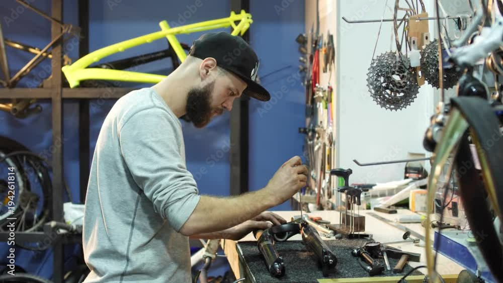 A man bike mechanic with a beard assembles a mountain bike in his workshop.
