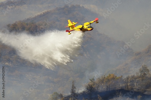 A yellow aircraft Canadair, water bomber or super scooper, in action on a forest fire.