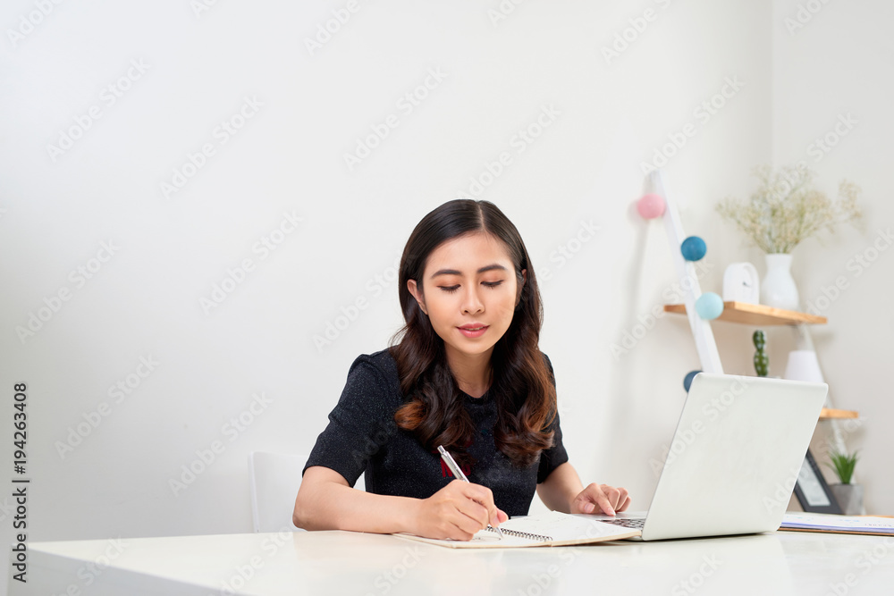 Woman studying with laptop and taking notes on a desktop at home. Woman studying with laptop and taking notes on a desktop at home.
