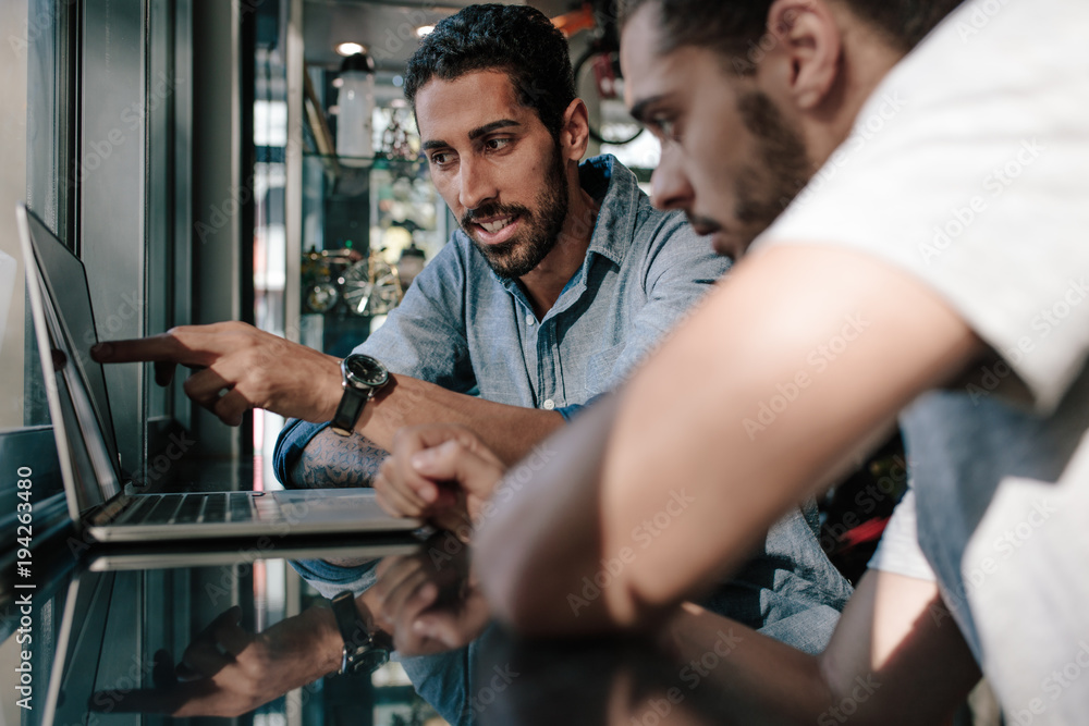 Sports shop owner discussing ideas with colleague using computer Sports shop owner discussing ideas with colleague using computer