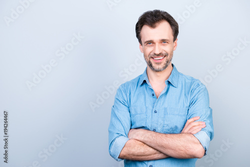 Portrait of confident concentrated cheerful excited glad with shiny beaming smile wearing light blue jeans shirt with rolled-up sleeves standing with folded arms isolated on gray background copyspace © deagreez