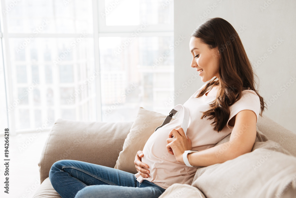 Smiling pregnant young woman holding headphones Smiling pregnant young woman holding headphones