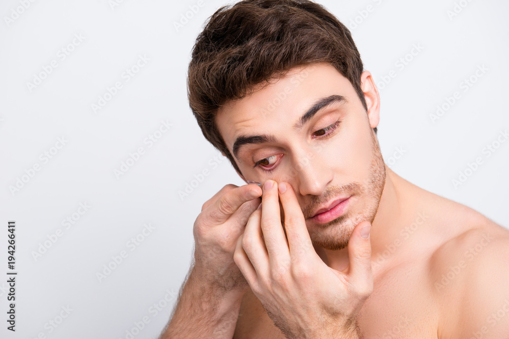 Fototapeta premium Close up portrait of young, attarctive, muscular man putting contact lenses in his eye over white background