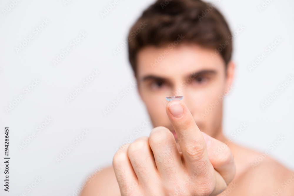Attractive, handsome man over white blurred background with copy space showing focused contact lens on forefinger Attractive, handsome man over white blurred background with copy space showing focused contact lens on forefinger