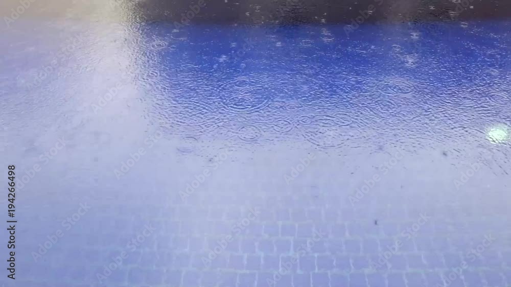 Rain dropping into the water in the blue swimming pool Rain dropping into the water in the blue swimming pool