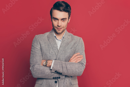 Portrait of stunning, confident, virile, harsh, manly, modern man looking at camera, having his arms crossed, isolated on red background