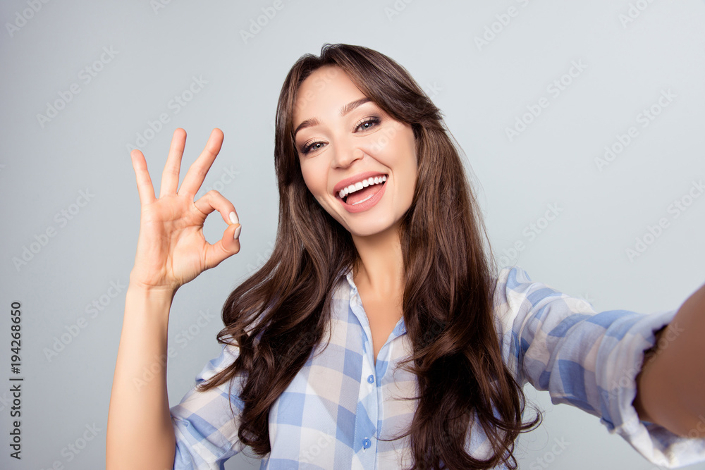 Close up picture of pretty, attractive, nice, cute woman with beaming smile shooting selfie, gesturing ok sign with fingers, having video call, standing over grey background Close up picture of pretty, attractive, nice, cute woman with beaming smile shooting selfie, gesturing ok sign with fingers, having video call, standing over grey background