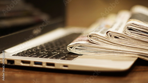 Newspapers and computer. Laptop and daily papers on the table. Fresh news by  paper or by electronic device, different ways of communication. Source of information, actual data on pages or on screen 