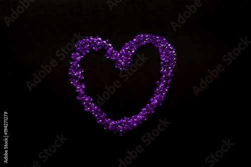 UV paetki scattered in the shape of the heart on a black background.  The decor for the party. photo