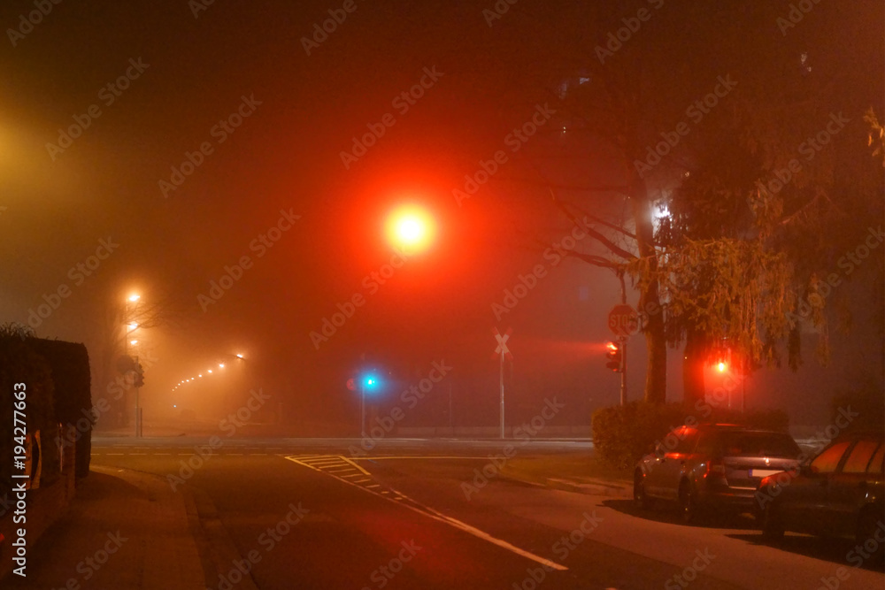 Straßenkreuzung nachts im Nebel / Eine Straße mit leuchtenden Straßenlaternen und einer Ampelkreuzung in der Nacht und im Nebel.