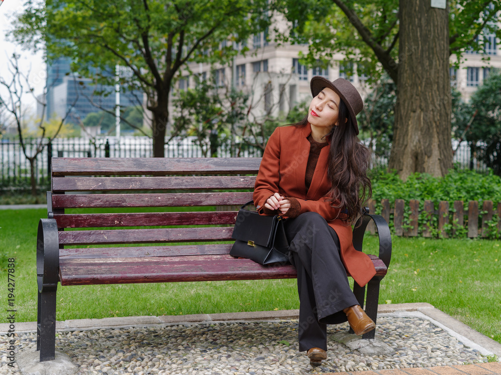 Beautiful young brunette woman sit on bench in park. Outdoor fashion portrait of glamour young Chinese cheerful stylish lady. Emotions, people, beauty and lifestyle concept. Beautiful young brunette woman sit on bench in park. Outdoor fashion portrait of glamour young Chinese cheerful stylish lady. Emotions, people, beauty and lifestyle concept.