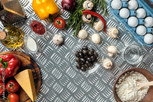 Food ingredients and spices for cooking pizza. Mushrooms, tomatoes, cheese, onion, oil, pepper, salt, egg, grater on metal background. Copy space. Top view